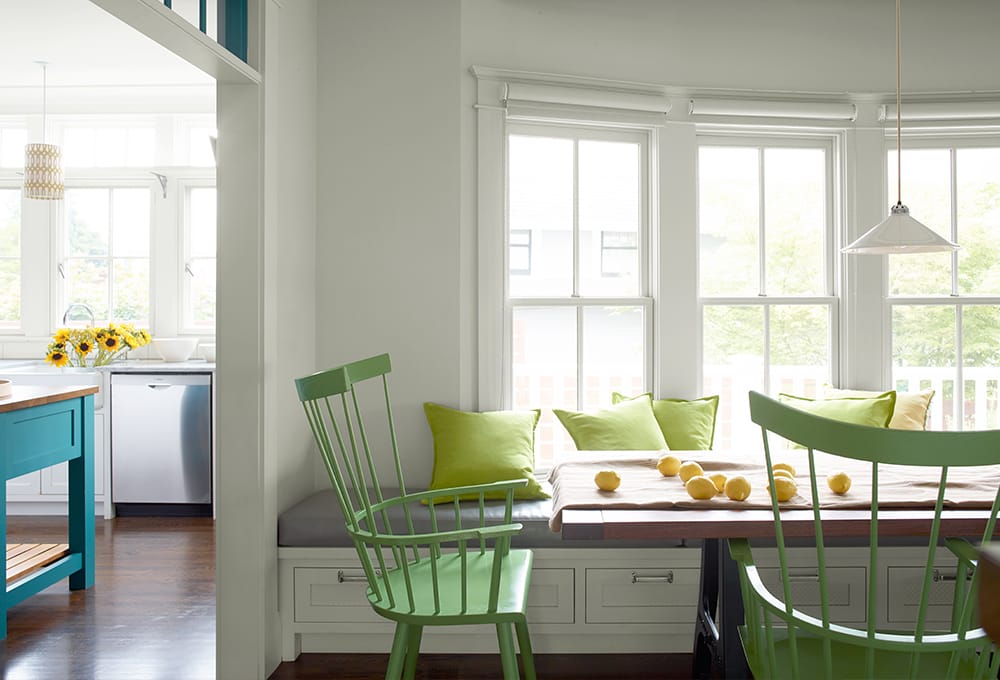 Dining room painted white, with large windows with white painted trim and bright green painted chairs.