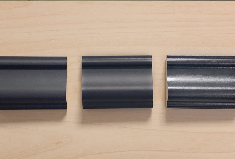Three pieces of trim each painted with a dark paint color in different sheens, matte, eggshell and gloss.