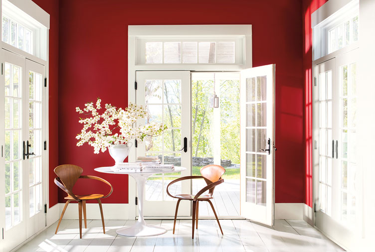A room with a bright red accent wall, large windows and doors with white painted trim.