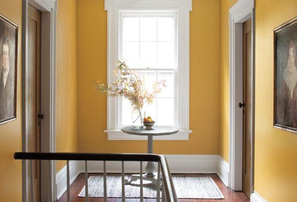 A hallway painted with a golden yellow, and a large window with white trim.