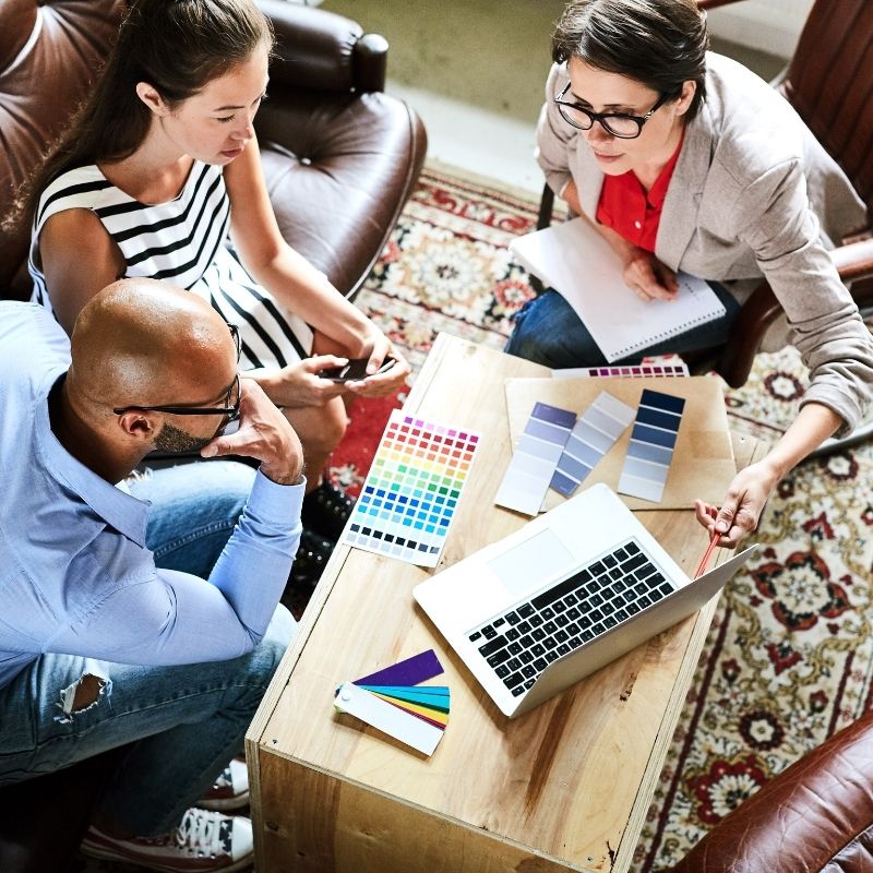 Three people sitting around a coffee table with a laptop and holding various paint swatches and Fan Decks.
