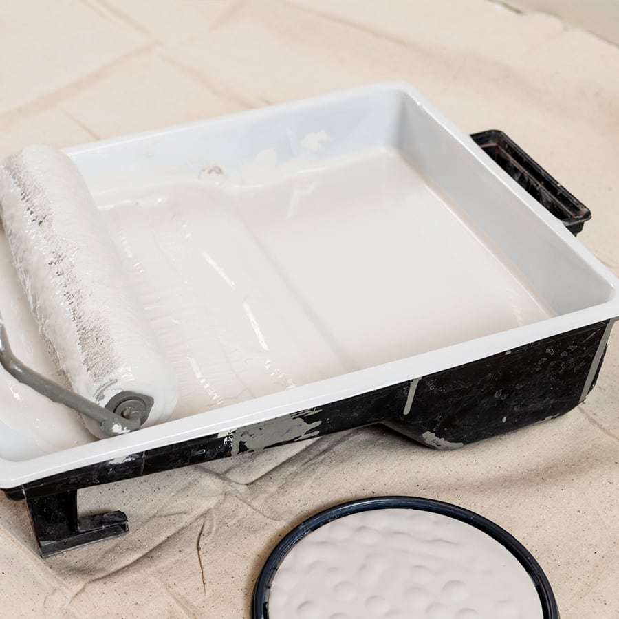 A paint tray with white paint inside and a paint roller and frame.